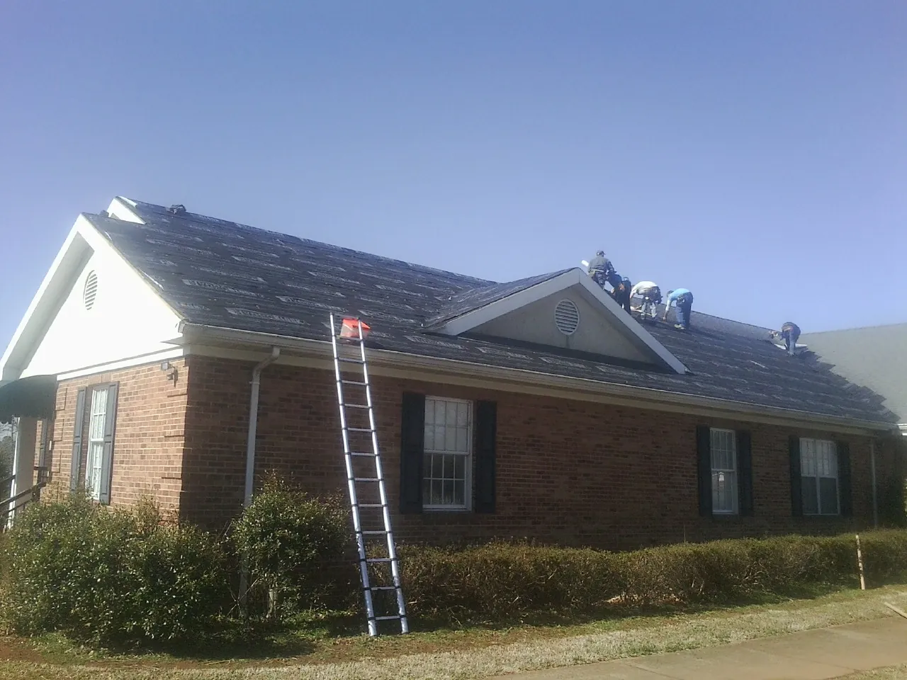 Crew tearing shingles off a brick ranch roof with a ladder set — Emergency Roof Repair work by our crew in Stevinson