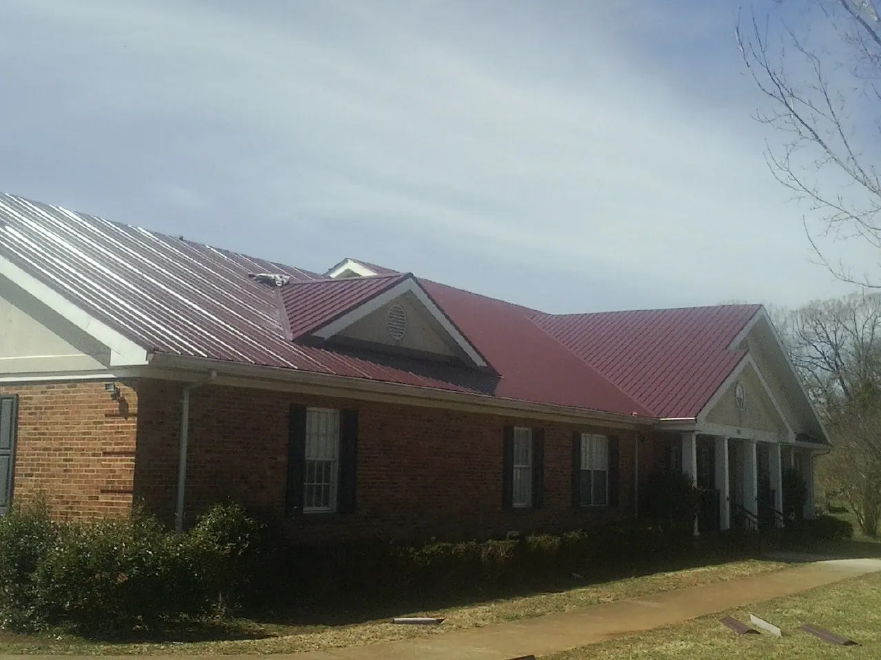 Red metal roof with gabled entries on a long brick building, from a Hail Damage Roof Repair job in Stevinson