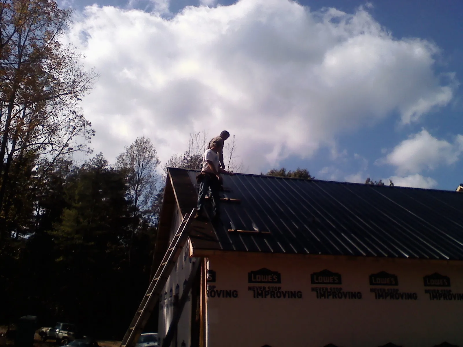 Roofer fastening dark metal panels high against a cloudy sky, from a Roof Inspection job in Stevinson