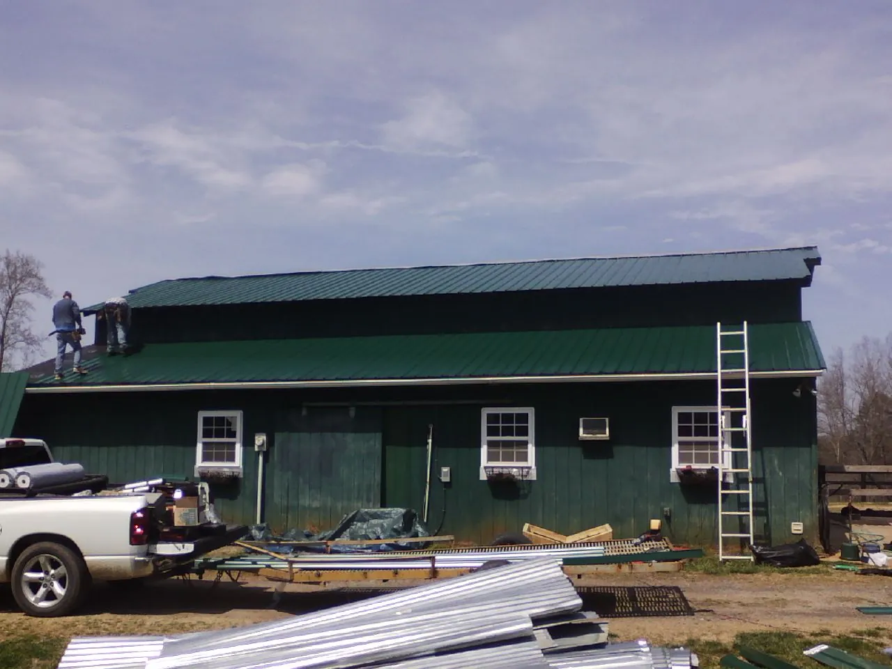 Crew installing green metal roofing on a large green barn in Stevinson