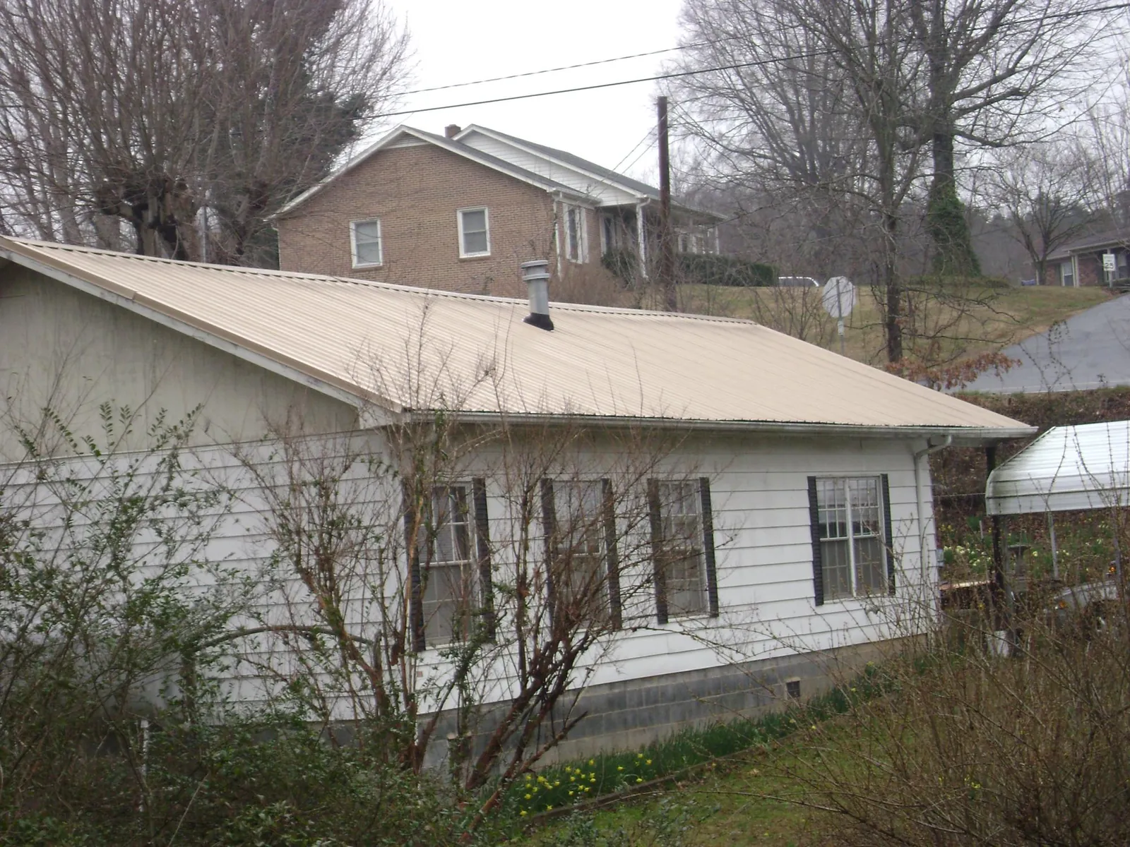 Tan metal roof on a white sided house set into a hillside — Commercial Roofing by Roofing Brothers in Stevinson